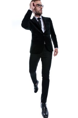 Siyah takım elbiseli zarif bir adam. Gözlük takıyor. Beyaz arka planda şık bir şekilde yürüyor.