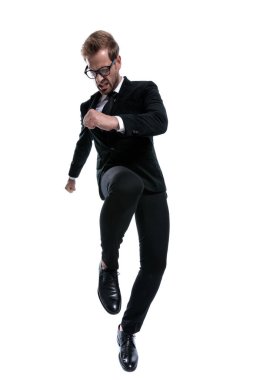 Siyah takım elbiseli kızgın dramatik adam bacağını kaldırıp tekmeliyor, beyaz arka planda üzgün bir surat yapıyor, tüm vücudunu.