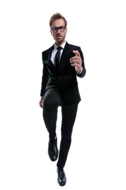 Siyah takım elbiseli dramatik adam dizini kaldırdı, beyaz arka planda yürüdü ve kaşlarını çattı.
