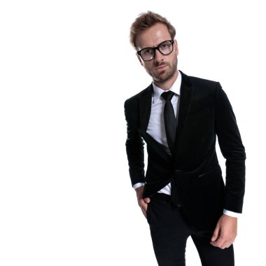 Siyah takım elbiseli genç adam el ele tutuşuyor, kaşlarını çatıyor ve beyaz arka planda yalnız poz veriyor.