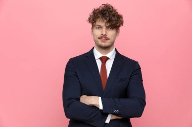 Lacivert takım elbiseli genç ve zarif iş adamı kollarını kavuşturup pembe sırıtıyor.