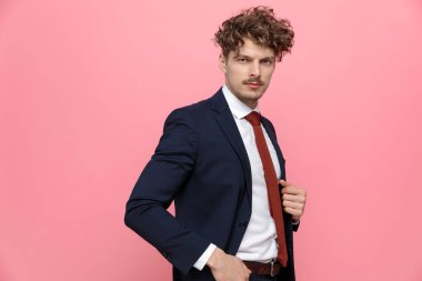 Ceplerinde el ele tutuşan, takım elbiseli, pembe arka planda yürüyen lacivert takım elbiseli zarif iş adamının yan görüntüsü.