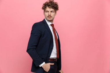 Mavili lacivert takım elbiseli şık bir adamın yan görünüşü, el ele tutuşması, yürümesi ve pembe arka planda poz vermesi.