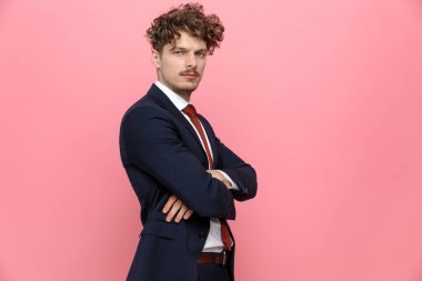 Mavili lacivert takım elbiseli, pembe arka planda duran ve poz veren genç ve zarif iş adamının yan görüntüsü.