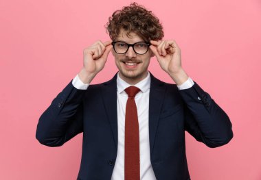 Lacivert takımlı, gözlüklü ve pembe arka planda gülümseyen mutlu bir adam.