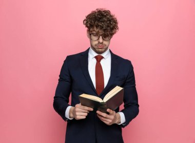 Lacivert takımlı, gözlüklü ve pembe arka planda kitap okuyan genç bir işadamı şok oldu.