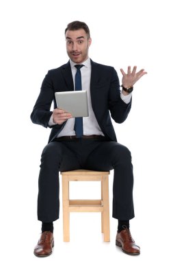 Harika bir iş adamı elinde tablet ve coşkuyla beyaz stüdyo arka planında bir sandalyede otururken...