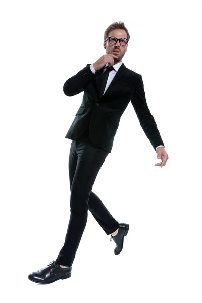 黒のスーツに身を包んだ格好いい男があごに触れ 仰向けに考え 白い背景の上を歩き 全身で — ストック写真