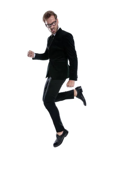 黒のスーツを着たクールな男が膝をついて飛び跳ねてお祝いし白い背景を見下ろし全身で — ストック写真