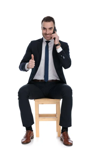 一个积极向上的商人在电话交谈 竖起大拇指 坐在白色工作室背景的椅子上大笑 — 图库照片