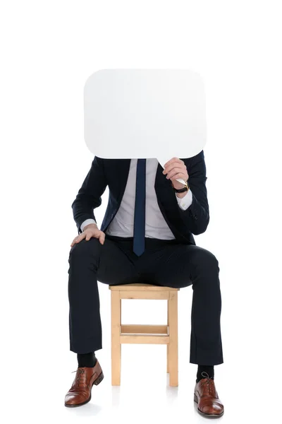 年轻的商人坐在白色画室背景的椅子上 满脸是空洞的演讲泡沫 — 图库照片