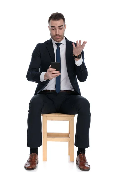 无精打采的商人坐在白色工作室背景的椅子上 一边打电话一边打手势 — 图库照片