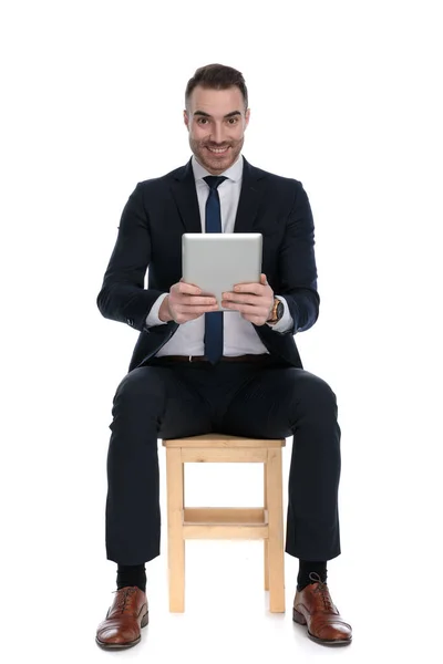 幸せなビジネスマン笑顔とタブレットを保持しながら 白いスタジオの背景に椅子に座って — ストック写真