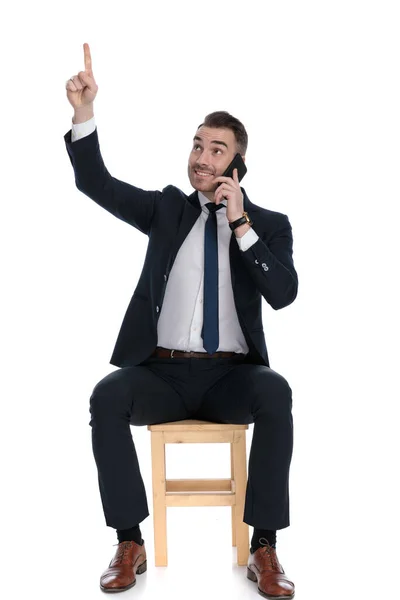 Empresário Positivo Falando Telefone Apontando Para Cima Sorrindo Enquanto Sentado — Fotografia de Stock