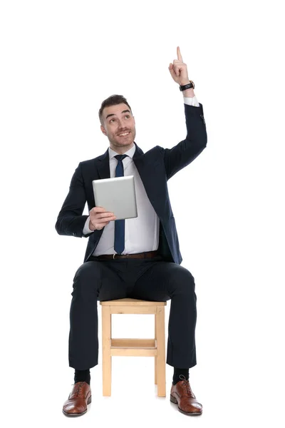 Empresário Feliz Apontando Para Cima Sorrindo Segurando Tablet Enquanto Sentado — Fotografia de Stock