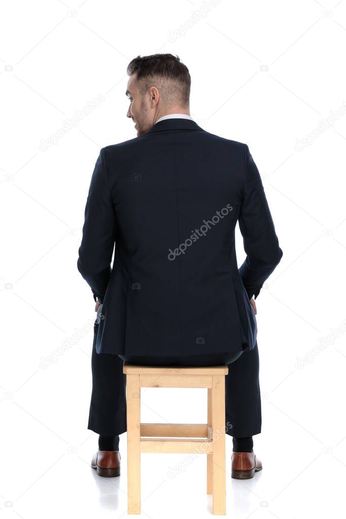 Back view of a businessman looking over his shoulder and sitting on a chair on white studio background