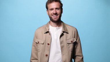 Genç, sıradan bir adam kameraya gülümsüyor ve mavi arka planda kollarını kavuşturuyor.