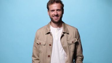 Yakışıklı, sıradan bir adam, geniş gülümsüyor ve iki eli de mavi arka planda.