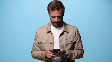 Yakışıklı, sıradan bir adam telefonuna bakıyor ve gülümsüyor. Sonra da mavi arka plandaki kameraya bakıyor.