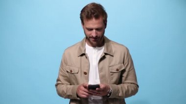 Seksi manken telefonuna mesaj atıyor, kameraya gülümsüyor ve mavi arka planda 