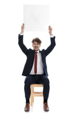 Seksi iş adamı boş bir reklam panosu tutuyor ve beyaz arka planda oturuyor.