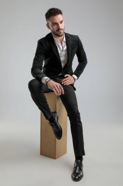 Yakışıklı iş adamı gözlerini kaçırıyor ve ellerini kucağında dinlendirirken gri arka plana bakıyor.