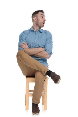 Beyaz stüdyo arka planında bir sandalyede otururken ellerini çaprazlayarak nefes nefese kalan zeki bir adam.