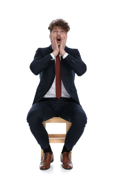 shocked businessman slapping his face, looking up and sitting on white background