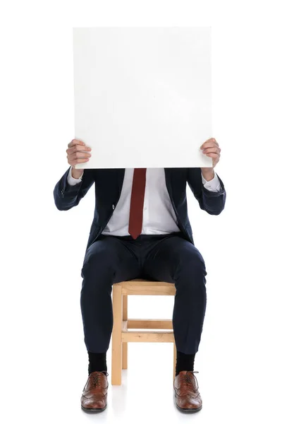 Empresário Escondendo Seu Rosto Atrás Cartaz Branco Sentado Contra Fundo — Fotografia de Stock