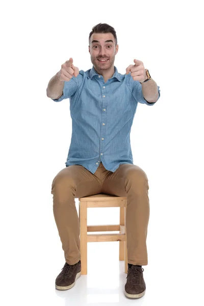 陽気スマートカジュアル男Pointing前方に両手で椅子に座っている間にホワイトスタジオの背景 — ストック写真