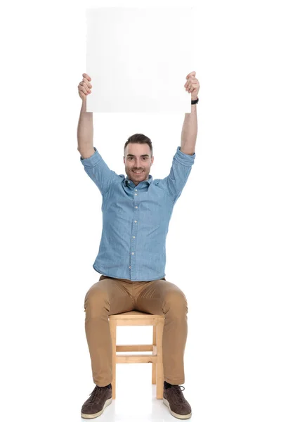 幸せなスマートなカジュアル男を保持ブランクビルボード上頭と笑顔上の椅子に座っている間にホワイトスタジオの背景 — ストック写真