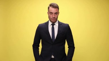 Genç işadamı elleri cebinde duruyor ve sarı arka planda sıcak bir gülümsemeyle gülümsüyor.