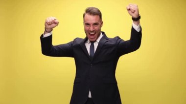 Genç yakışıklı iş adamı iki elini de kaldırıyor ve sarı arka plandaki başarıları kutluyor.