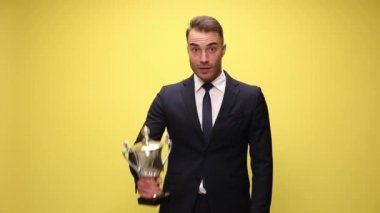 Heyecanlı iş adamı fincanını sunuyor ve sarı arka planda başarıları kutluyor.