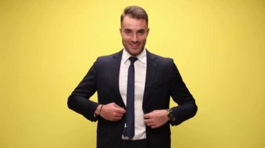 Çekici iş adamı ceketini kapatıyor ve sarı arka plandaki saatini kontrol ediyor.