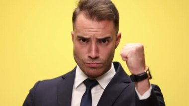 Yakışıklı bir iş adamının yumruğunu sıkıca kaldırıp kamerayı işaret etmesi ve sarı arka planda dövülmüş bir tabela göstermesi.