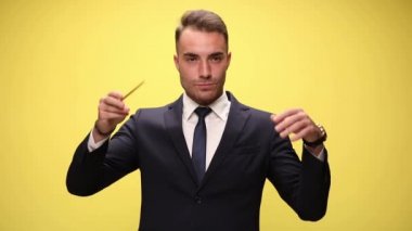 Genç müzisyen takım elbiseli ve kravatlı işadamı sarı arka planda bir orkestra yönetiyor.