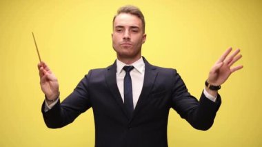 Çekici müzisyen iş adamı. Sarı arka planda sert bir tavırla orkestra yönetiyor.