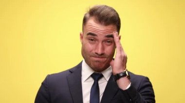 Alnını ovuşturan ve sarı arka plana bakan bir iş adamına yaklaş.