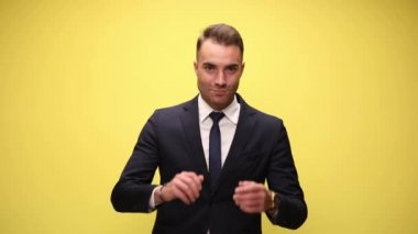 Çekici iş adamı, sarı arka planda geniş bir gülümseme ve açık kollarla selamlıyor.