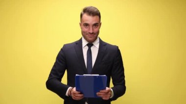 Çekici iş adamı notlarını panosundan okuyor, gülümsüyor ve sarı arka plandaki kameraya işaret ediyor.