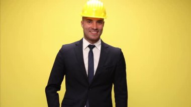 Çekici iş adamı bir eli cebinde, kask takıyor ve sarı arka planda 
