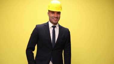 Genç işadamı kask takıyor, bir eli cebinde ve diğeriyle 