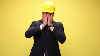 Şok olmuş iş adamı sarı bir kask takıyor, yüzüne tokat atıyor ve sarı arka planda olanlara inanamıyordu.