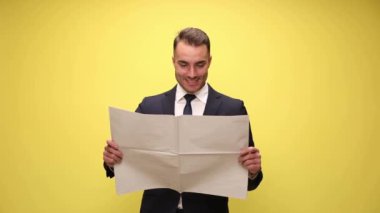 Mutlu iş adamı gazete okuyor, gülümsüyor ve sarı arka planda başını sallıyor.