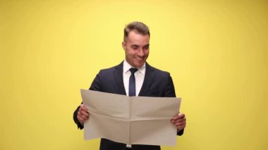 Sarı arka planda dikilmiş gazete okuyan seksi iş adamı.