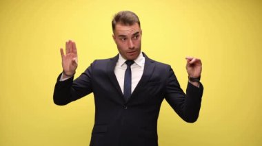 İş adamı sarı arka planda konuşan iki eliyle taklit yapıyor.