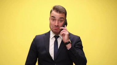Mutlu sürpriz iş adamı telefonda konuşuyor, geniş gülümsüyor ve sarı arka planda heyecanlanıyor.