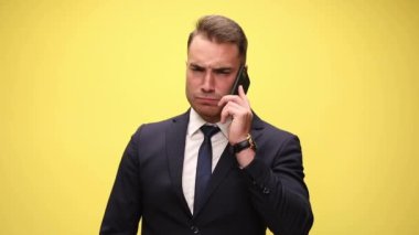 Seksi iş adamı telefonda konuşuyor, sonra çok sinirleniyor, aramayı bitiriyor, sarı arka planda yumruğunu telefona gösteriyor.