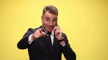 Çekici iş adamı telefonda konuşuyor, kamerayı işaret ediyor, sarı arka planda bana işaret ve yumruk tokalaşması işareti yapıyor.